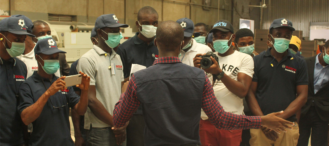 A group of men in Bosch shirts listens to a speaker in a workshop setting.