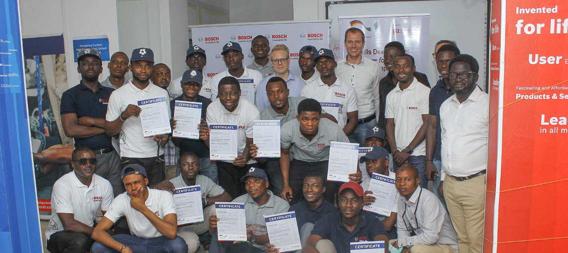 Group of people holding Bosch certificates, smiling, in a bright indoor setting.