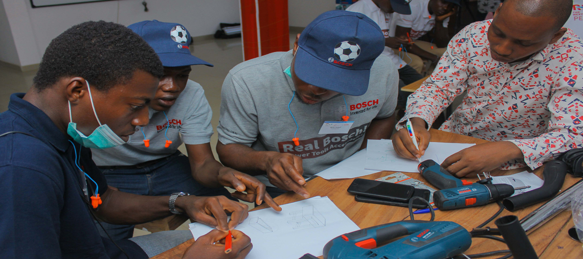 Four men in Bosch shirts sketching designs at a table with tools and papers.