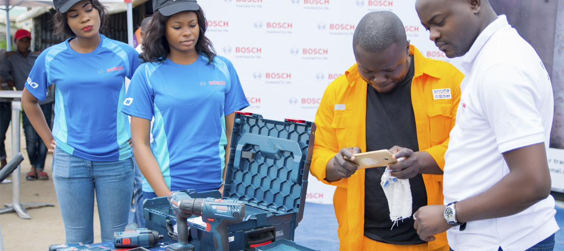 Four people interact near Bosch tools displayed on a table at an outdoor event.