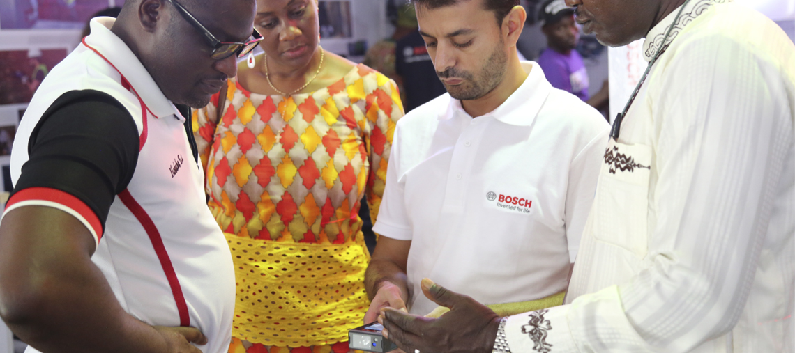 Four people engage with Bosch tools at a colorful exhibition, focused on a device.
