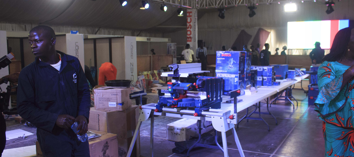 A man holds a water bottle near Bosch tools displayed on tables in an event space.
