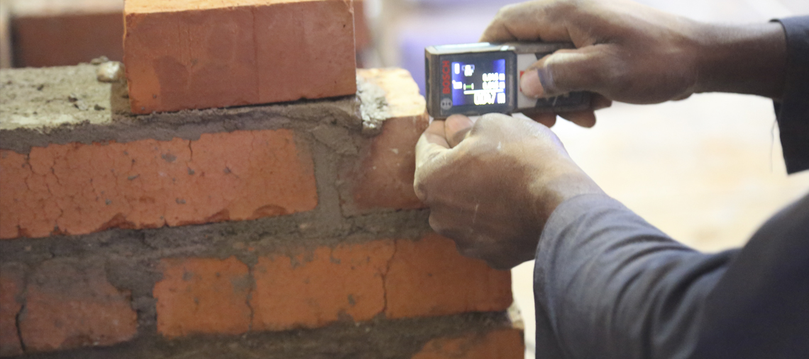 A person uses a measuring tool on a brick wall under construction.