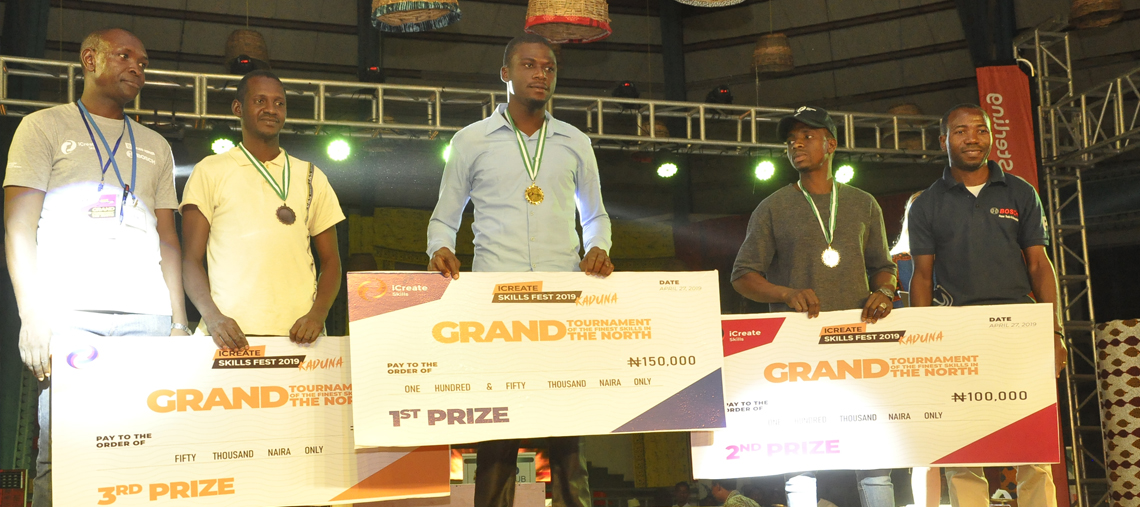 Four men hold large prize checks at a skills competition, smiling with medals around their necks.