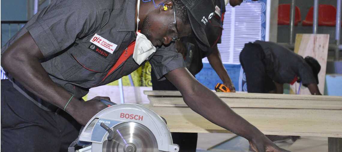 A worker uses a Bosch circular saw on wooden boards in a workshop setting.