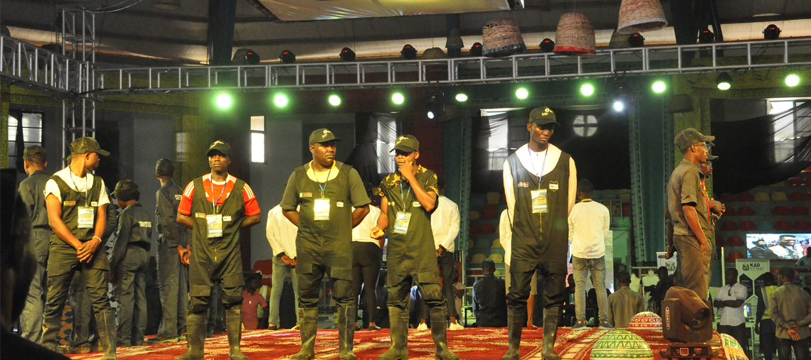 Five men in black overalls stand on stage under green lights, engaged in an event.