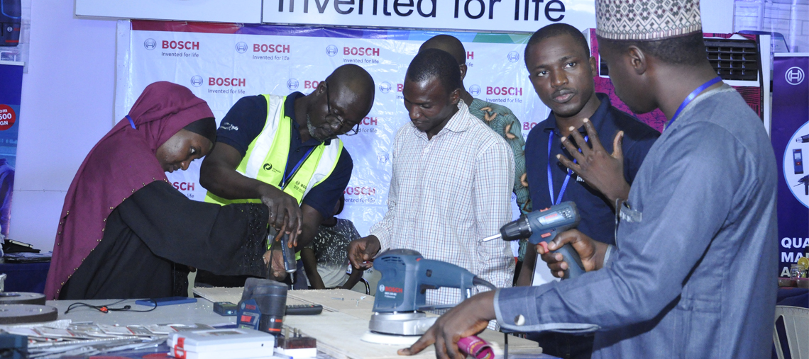 People in Bosch gear engage with tools at a workshop table, showcasing professional equipment.