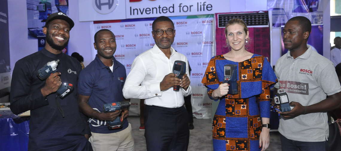 Four people hold Bosch tools, smiling, in a brightly lit exhibition space with branding.