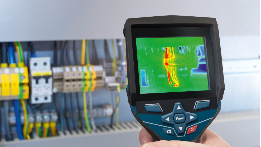 Een Bosch thermisch meetapparaat wordt vastgehouden voor een elektrisch paneel met gekleurde kabels.