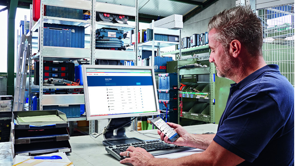 Een man in een blauwe shirt werkt aan een computer met gereedschap op de achtergrond.