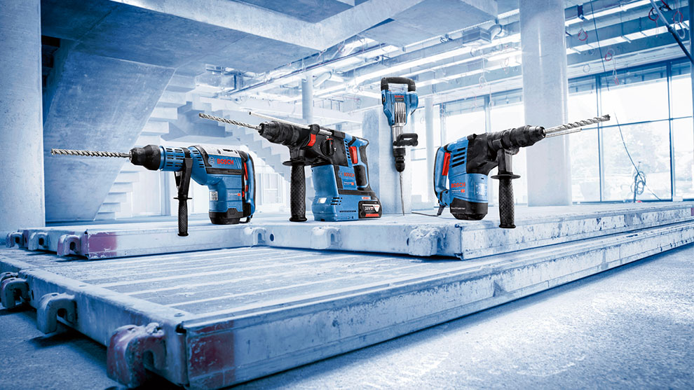 Vier blauwe Bosch Professional gereedschappen op een betonnen vloer in een bouwomgeving.