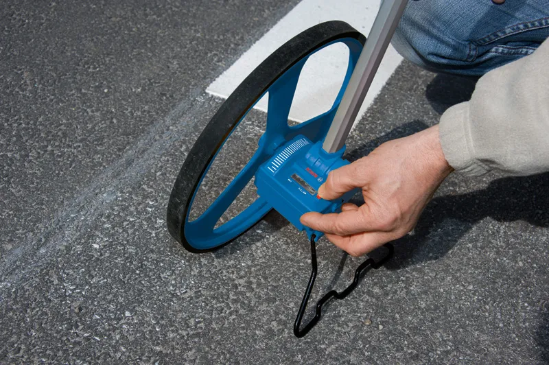 Een persoon meet de afstand over de weg met een blauw meetwiel op het trottoir.