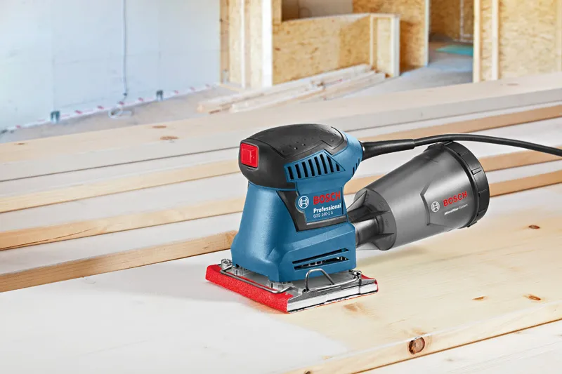 Excenterschuurmachine rustend op houten planken in een werkplaats.