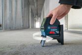 Een persoon stelt een laserwaterpas in op een betonnen vloer in een onafgewerkte gang.
