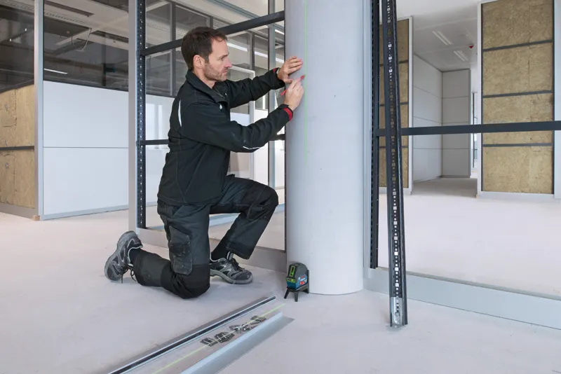 Een persoon met veiligheidsuitrusting markeert een betonnen pilaar met behulp van een laserwaterpas.