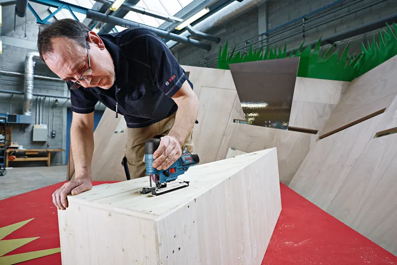 In een werkplaats gebruikt iemand een snoerloze decoupeerzaag om hout te zagen.