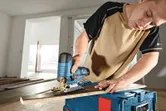 Een persoon zaagt een houten plank met een draadloze decoupeerzaag op een gereedschapskist.