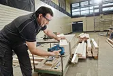 Een persoon met veiligheidsuitrusting zaagt hout met een accu-decoupeerzaag in een werkplaats.