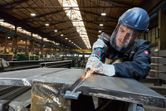 Een persoon die veiligheidsuitrusting draagt, slijpt metaal met een elektrisch gereedschap in een fabriek.