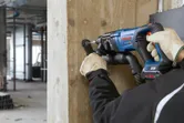 Een persoon die veiligheidsuitrusting draagt, boort met een elektrisch gereedschap in een betonnen pilaar.