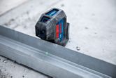Laserwaterpas projecteert een groene lijn op een metalen rail op een betonnen vloer.