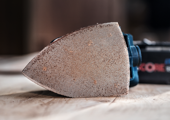 Detailweergave van een schuurzool bevestigd aan een elektrisch gereedschap op een houten oppervlak.