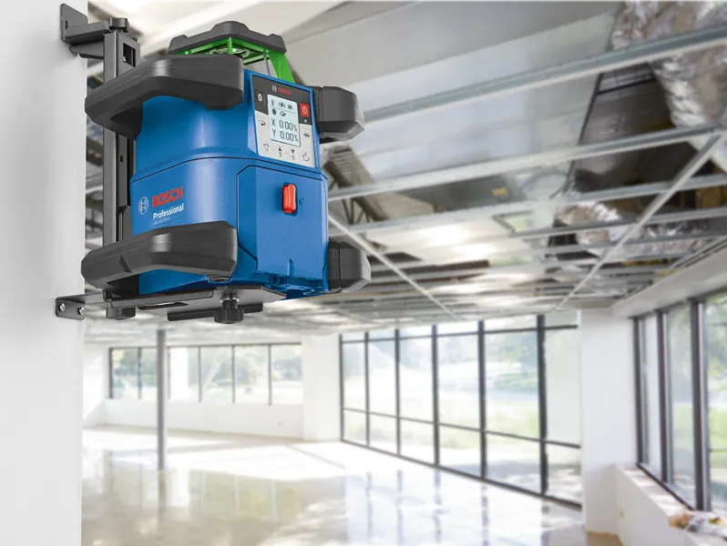 Laserwaterpas aan de muur gemonteerd in een lichte ruimte met een open plafond.