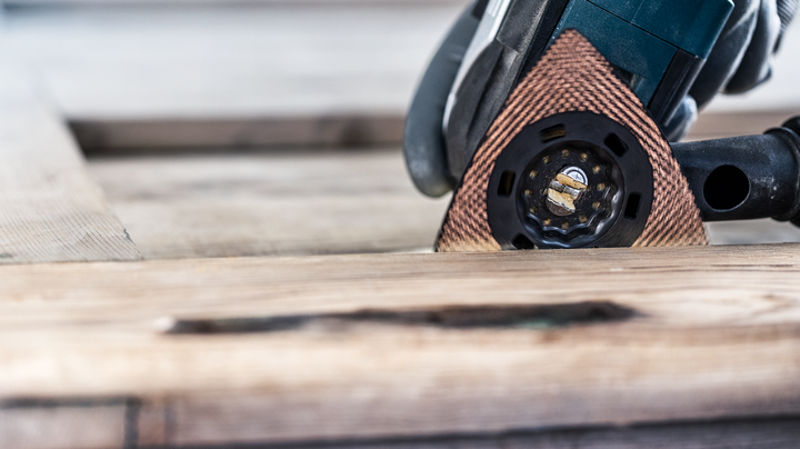 Persoon met veiligheidsuitrusting die hout schuurt met een multitool.