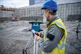 Een persoon die veiligheidsuitrusting draagt, bedient een laserwaterpas op een bouwterrein.