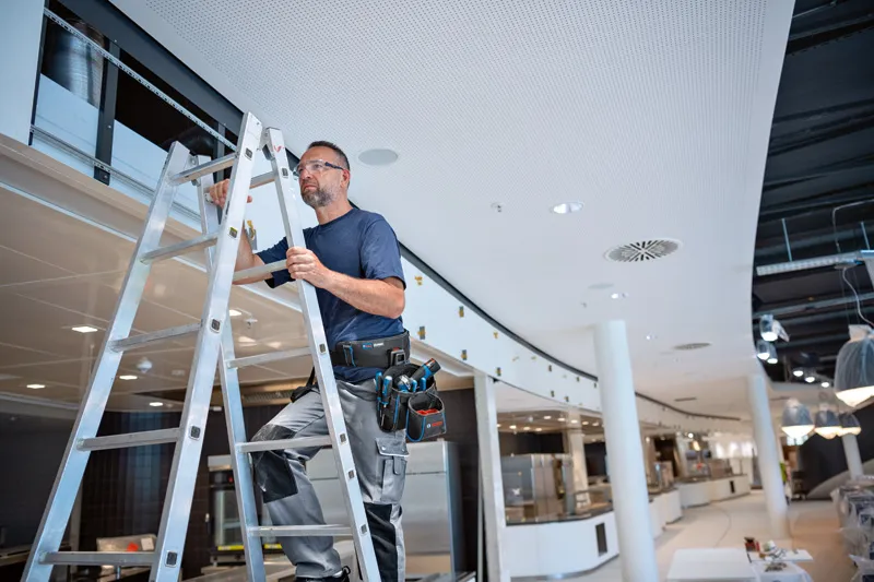 Een persoon die veiligheidsuitrusting draagt, staat op een ladder en maakt gebruik van een gereedschapsriemcombinatieset.