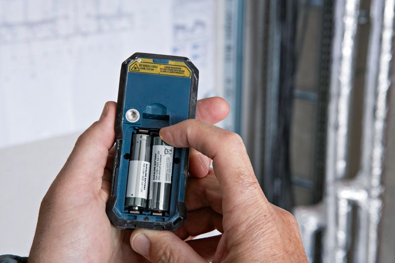 Persoon plaatst batterijen in de achterkant van een lasermeetapparaat.