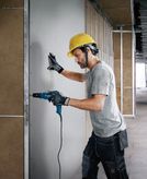 Een persoon met veiligheidsuitrusting boort in gipsplaat in een gebouw in aanbouw.