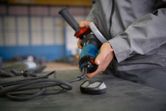 Een persoon die veiligheidsuitrusting draagt, sluit een elektrisch gereedschap aan op een werkbank.