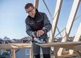Een persoon met veiligheidsuitrusting zaagt hout met een snoerloze cirkelzaag op een bouwplaats.