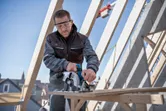 Een persoon met veiligheidsuitrusting zaagt multiplex met een cirkelzaag op een bouwplaats.
