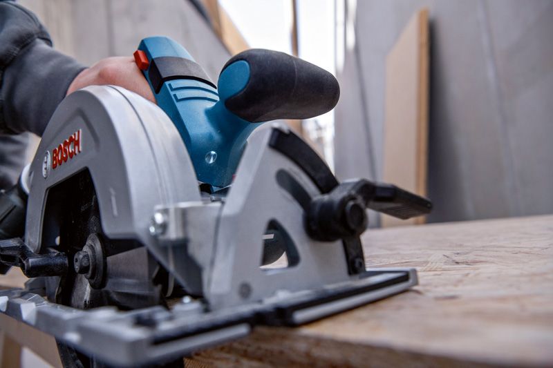 Een persoon gebruikt een cirkelzaag om een houten plank in een werkplaats te zagen.