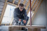 Een persoon die veiligheidsuitrusting draagt, zaagt een houten balk door met een cirkelzaag.