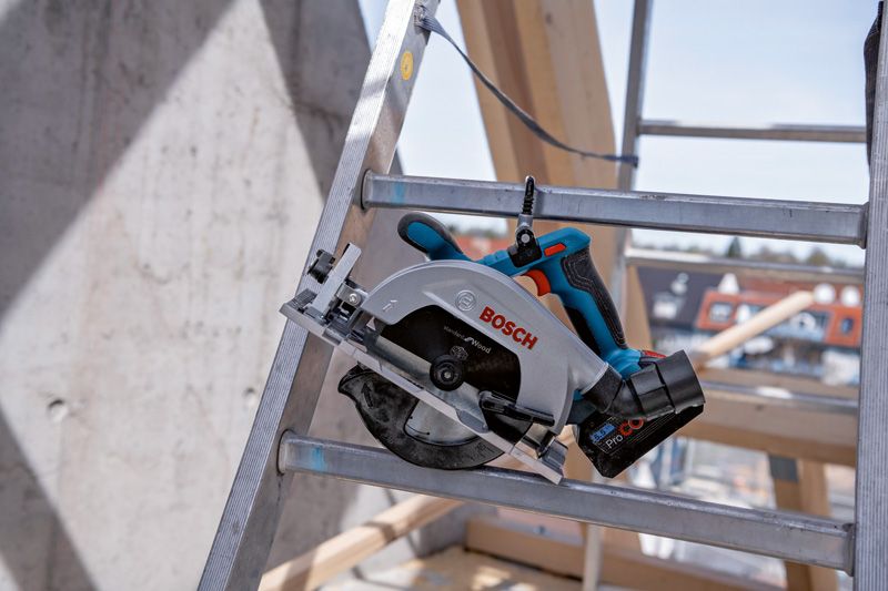 Een draadloze cirkelzaag staat op een metalen ladder op een bouwterrein.