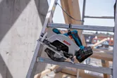 Een draadloze cirkelzaag staat op een metalen ladder op een bouwterrein.