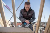 Een persoon die veiligheidsuitrusting draagt, gebruikt een snoerloze cirkelzaag op een houten plank.