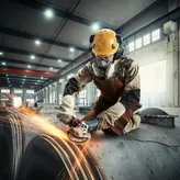 In een industriële omgeving slijpt iemand die veiligheidsuitrusting draagt metaal, waardoor vonken ontstaan.
