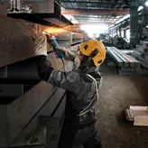 Een persoon die veiligheidsuitrusting draagt, slijpt een metalen balk, waardoor felle vonken ontstaan.