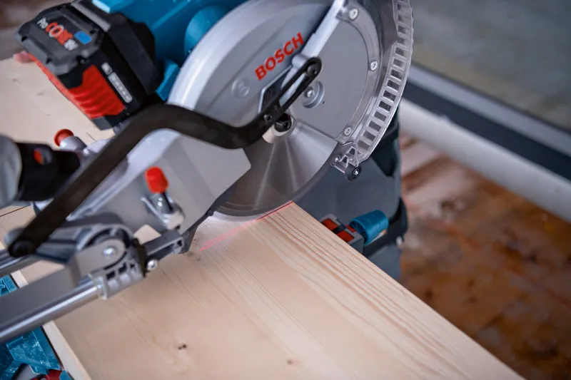 Een verstekzaag met lasergeleider zaagt een houten plank op een werkbank.