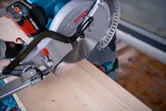 Een verstekzaag met lasergeleider zaagt een houten plank op een werkbank.