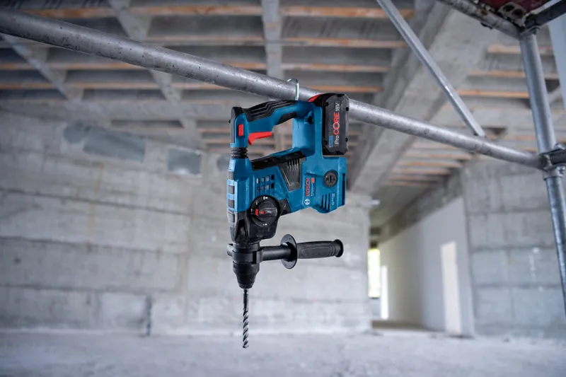 Draadloze boorhamer hangt aan zijn handvat aan een metalen steiger in een betonnen gebouw.