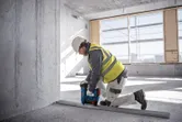 Een persoon die veiligheidsmateriaal draagt, bevestigt met een draadloze betonspijkermachine een metalen spoor aan de vloer.