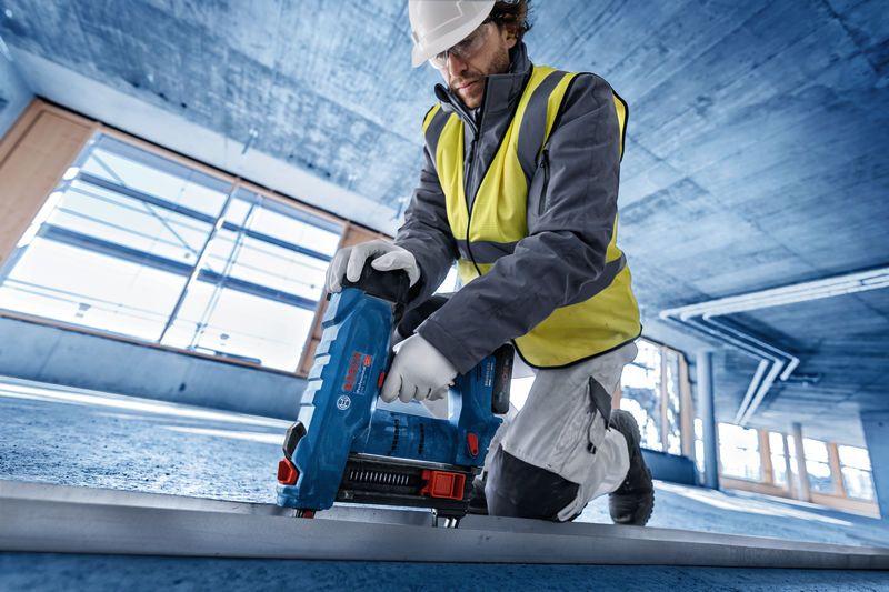 Een persoon die veiligheidsuitrusting draagt, bedient een blauwe boorkern op een betonnen vloer.