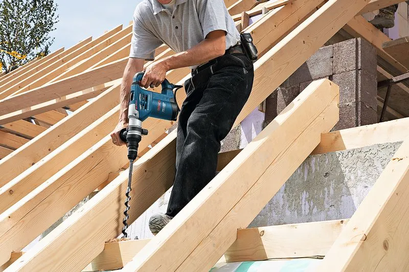 Een persoon die in een houten balk op een dakconstructie boort, draagt geen veiligheidsuitrusting.