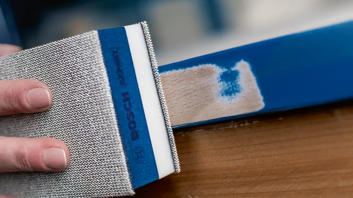 Persoon schuurt een blauw geverfd houten oppervlak.