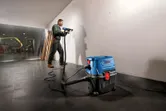 Een persoon met veiligheidsuitrusting boort met behulp van een natte of droge stofzuiger in een muur.